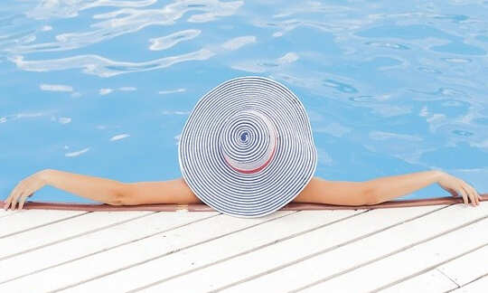 Stuff In Sunscreen May Play A Part In Breast Cancer Women laying in the pool with her arms on the edge, wearing a sun hat