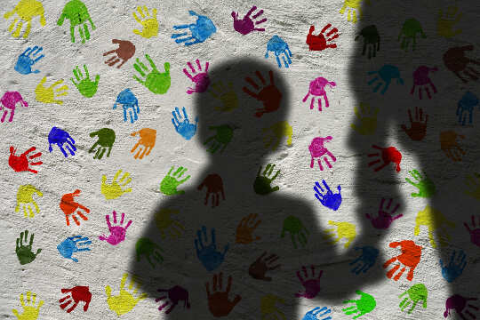 Giving Away Your Power? Going From Fear to Empowerment silhouette of a boy holding an adult's hand, with a background of colorful handprints on the wall