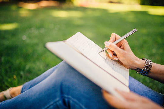 Valuable Habits and Mindsets to Re-invent Your Life a person sitting outside on the grass writing in a notebook