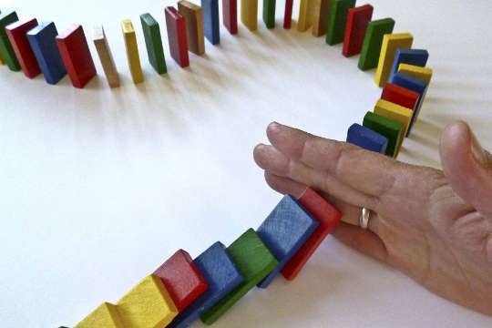 Today's Inspiration: October 27, 2022 a hand holding back a barricade of dominoes from falling