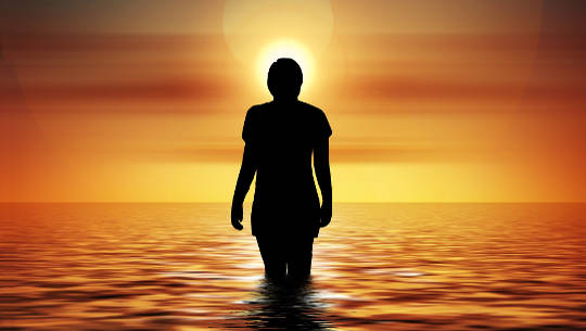 Understanding 5th Dimension Consciousness and the Divine Feminine Within Us woman standing in the ocean looking at the rising sun