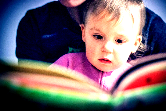 Ready to Birth the New World? a child sitting on his mother's lap and reading from a book