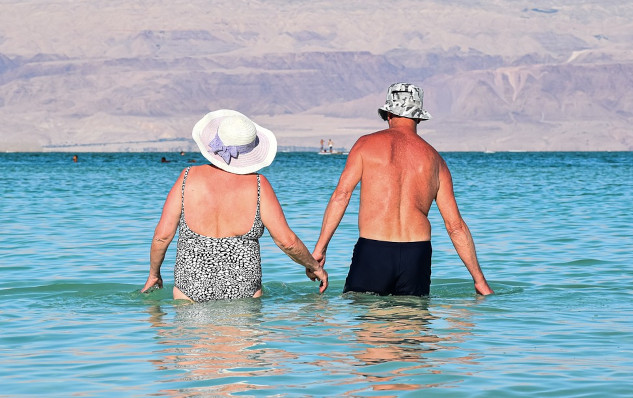 an older woman and man holding hands and walking into the calm waters of the ocean