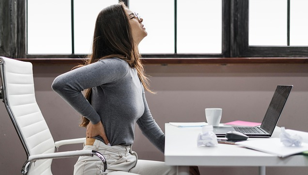 How To Treat Lower Back Pain Without Drugs Woman sitting at a computer with her hand on her aching back. Image by fairpharma from Pixabay.