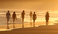 people walking barefoot in the water's edge on the beach