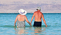 an older woman and man holding hands and walking into the calm waters of the ocean