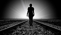 silhouette of a person walking on a railroad track towards the light